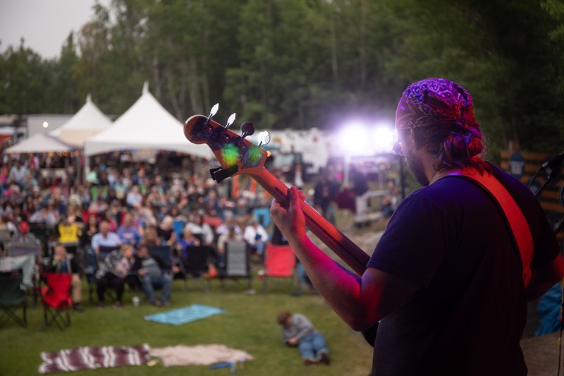 A guitarist plays to a large crowd in front of him outdoors.